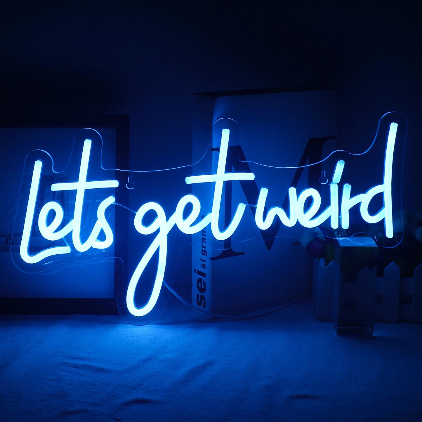De afbeelding toont een levendig "Let's Get Weird" LED-neonbord dat aan een muur is bevestigd.