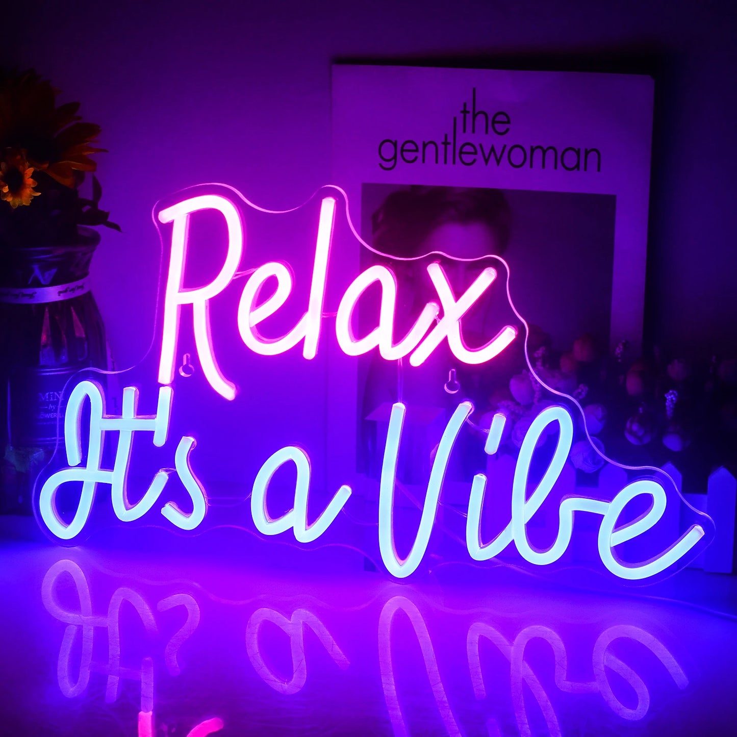 De afbeelding toont een levendig LED-neonbord met de tekst "Relax It's a Vibe" in een stijlvol, cursief lettertype.