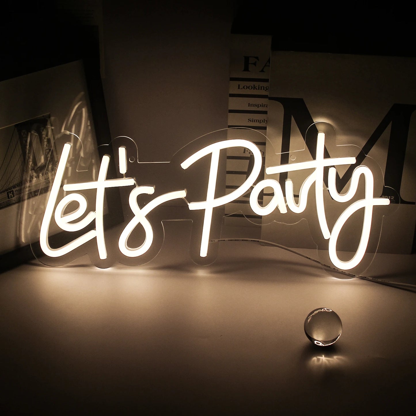 Er wordt een levendig "Let's Party" LED-neonbord tentoongesteld, met opvallende, cursieve letters.