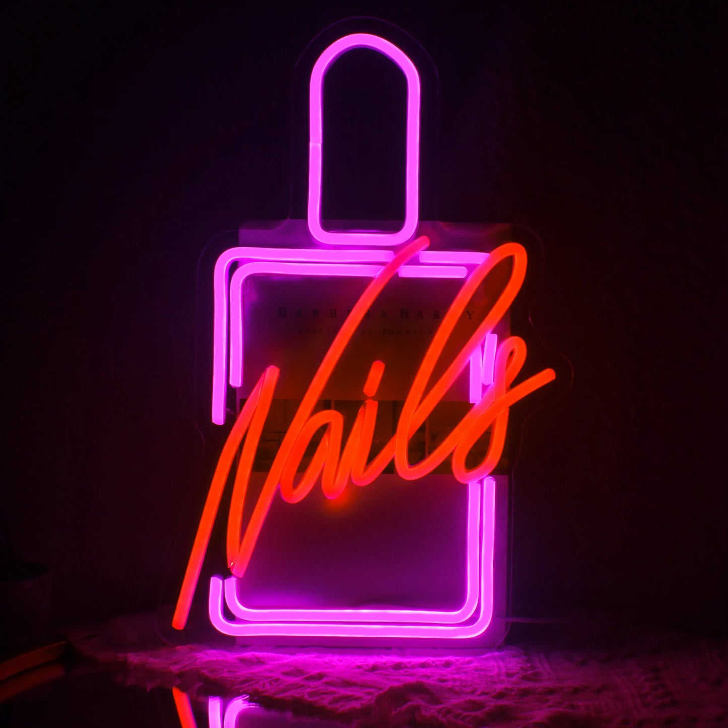 De afbeelding toont een levendig LED-neonbord waarop het woord "Nails" in een stijlvol, cursief lettertype staat.