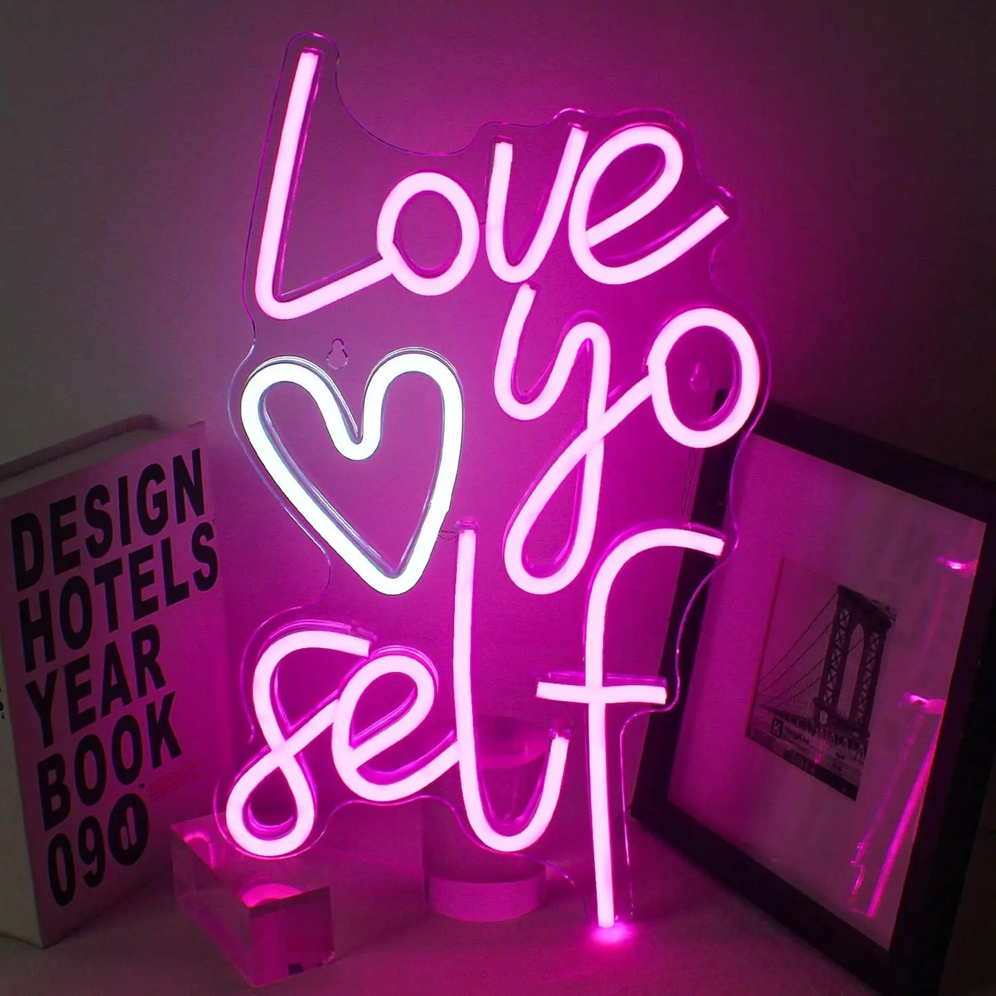 Een levendig "Love Yo Self" LED-neonbord is te zien tegen een eenvoudige, donkere achtergrond.
