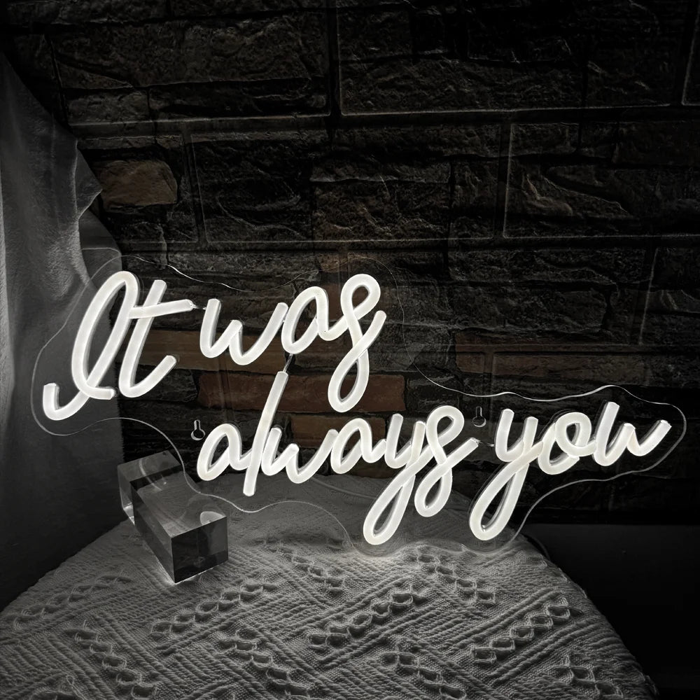 De afbeelding toont een levendig LED-neonbord met de tekst "It Was Always You" in een stijlvol, cursief lettertype.