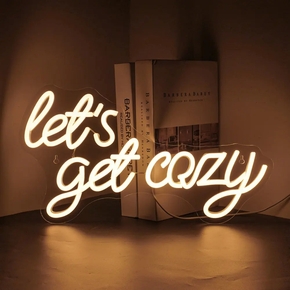 De afbeelding toont een levendig LED-neonbord met de tekst "Let's Get Cozy" in een warm, uitnodigend lettertype.