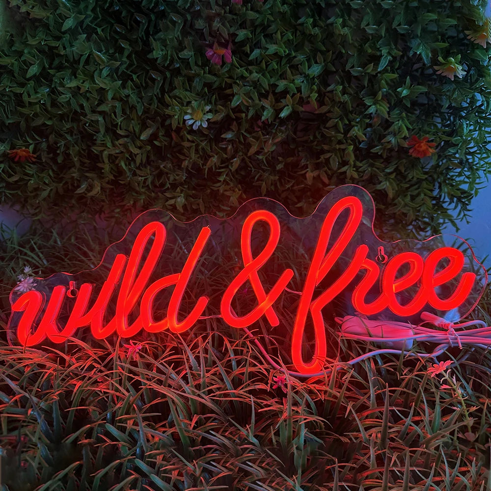 De afbeelding toont een levendig LED-neonbord met de tekst "Wild & Free" in een stijlvol, cursief lettertype.
