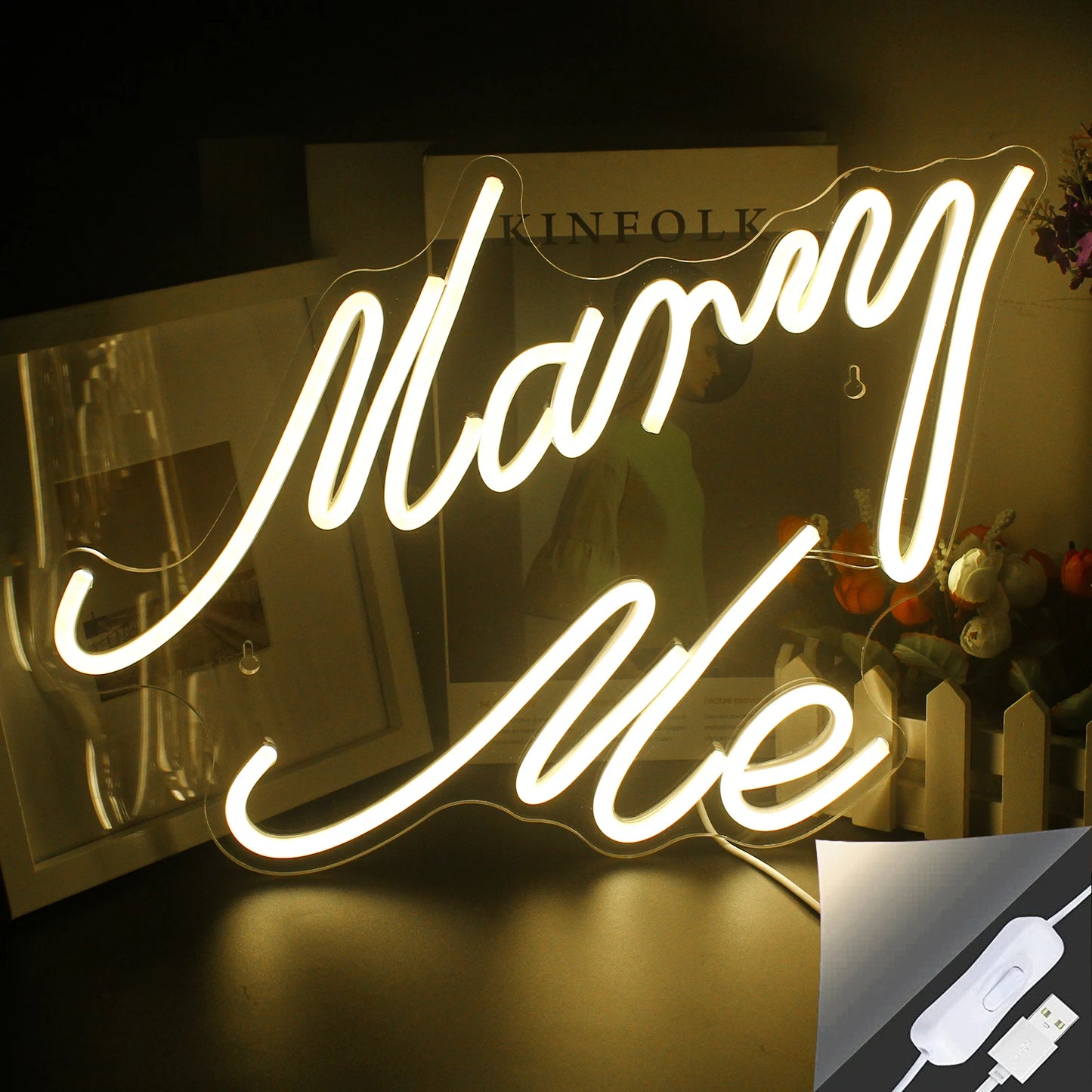 Er is een LED-neonreclame met de tekst "Marry Me" te zien, die fel oplicht in een warmwitte tint.