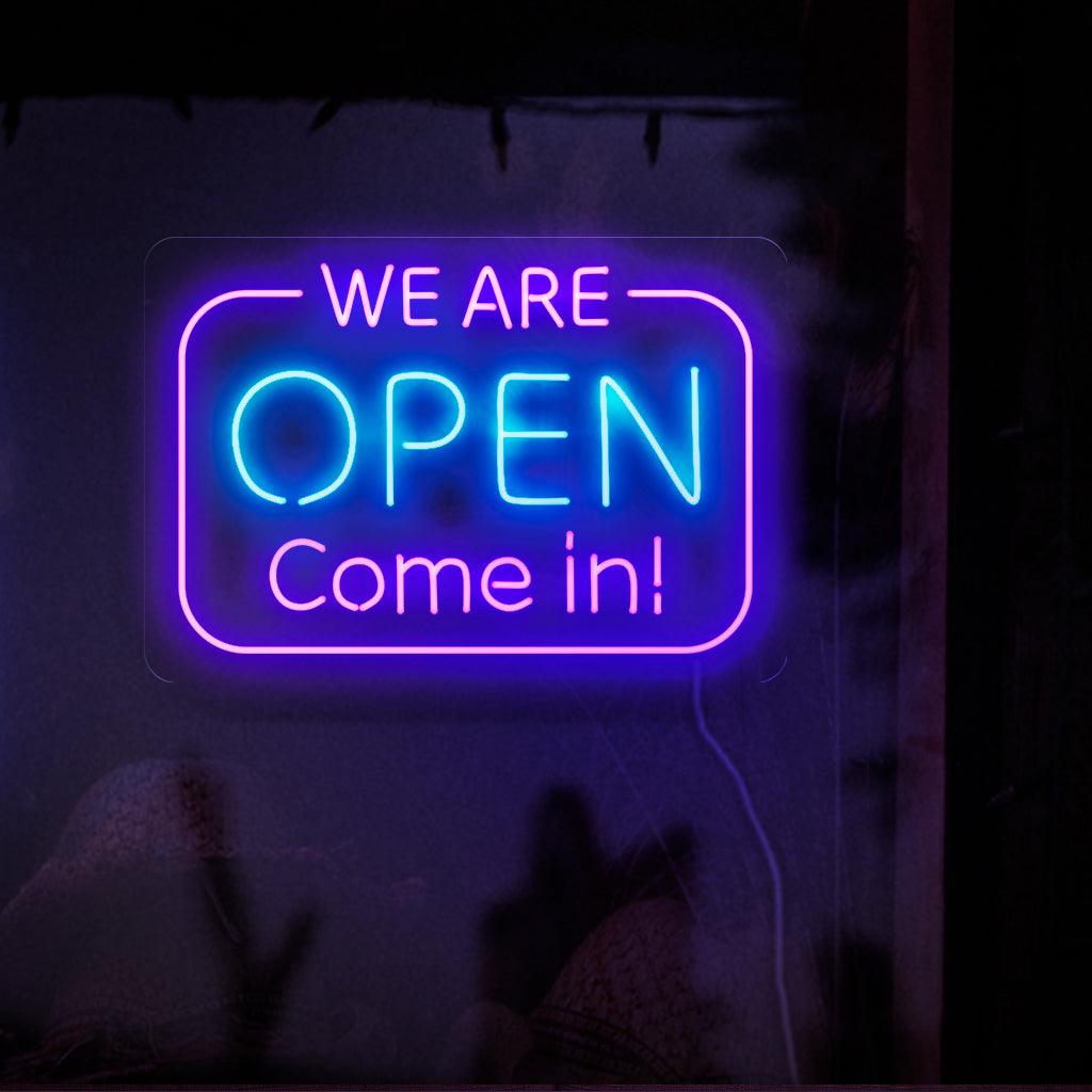 Een opvallend neonbord met opvallende, oplichtende letters die de tekst 'Wij zijn open. Kom binnen' vormen.