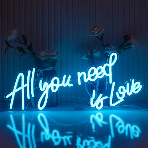 Op de afbeelding staat een opvallend LED-neonbord waarop de tekst "All You Need Is Love" in een stijlvol, cursief lettertype staat.