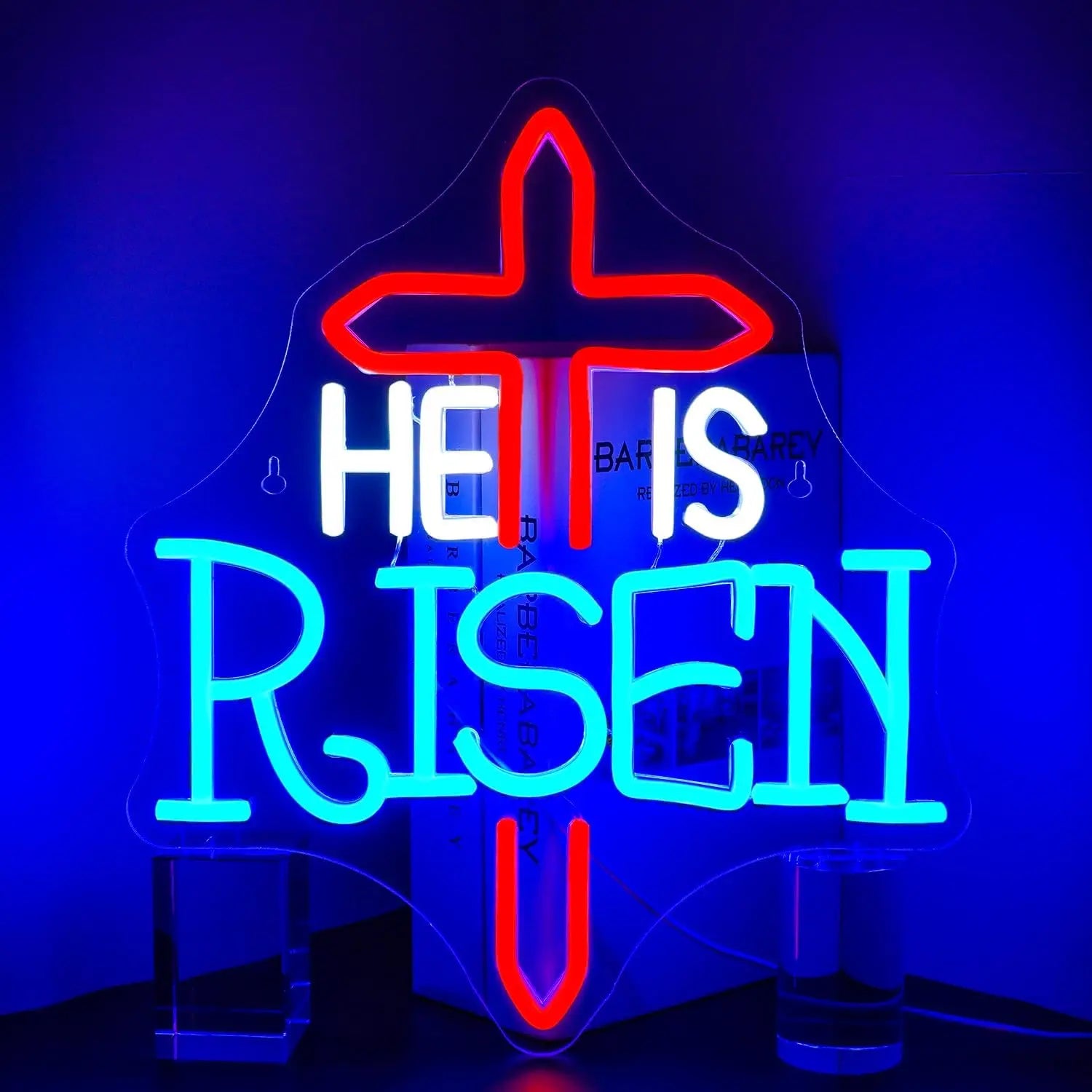 The image features a vibrant "He Is Risen" LED neon sign glowing in bold, warm hues.