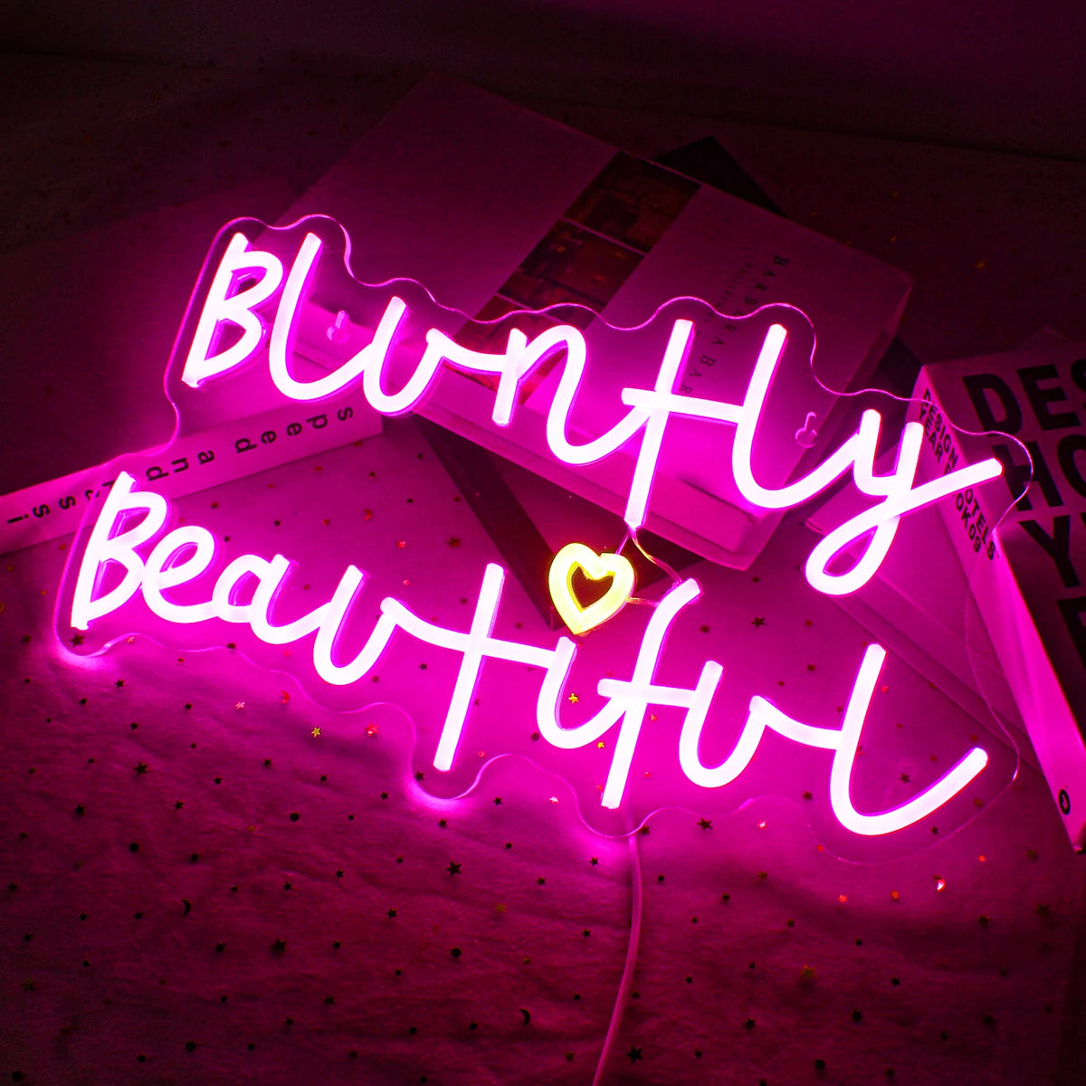 Op de afbeelding staat een levendig, handgemaakt LED-neonbord met de tekst 'Bluntly Beautiful'.