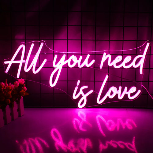 Op de afbeelding staat een levendig LED-neonbord met de tekst "All You Need is Love" in elegante, cursieve letters.
