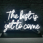 De afbeelding toont een levendig, handgemaakt LED-neonbord met de tekst "The Best is Yet to Come" in een stijlvol, cursief lettertype.