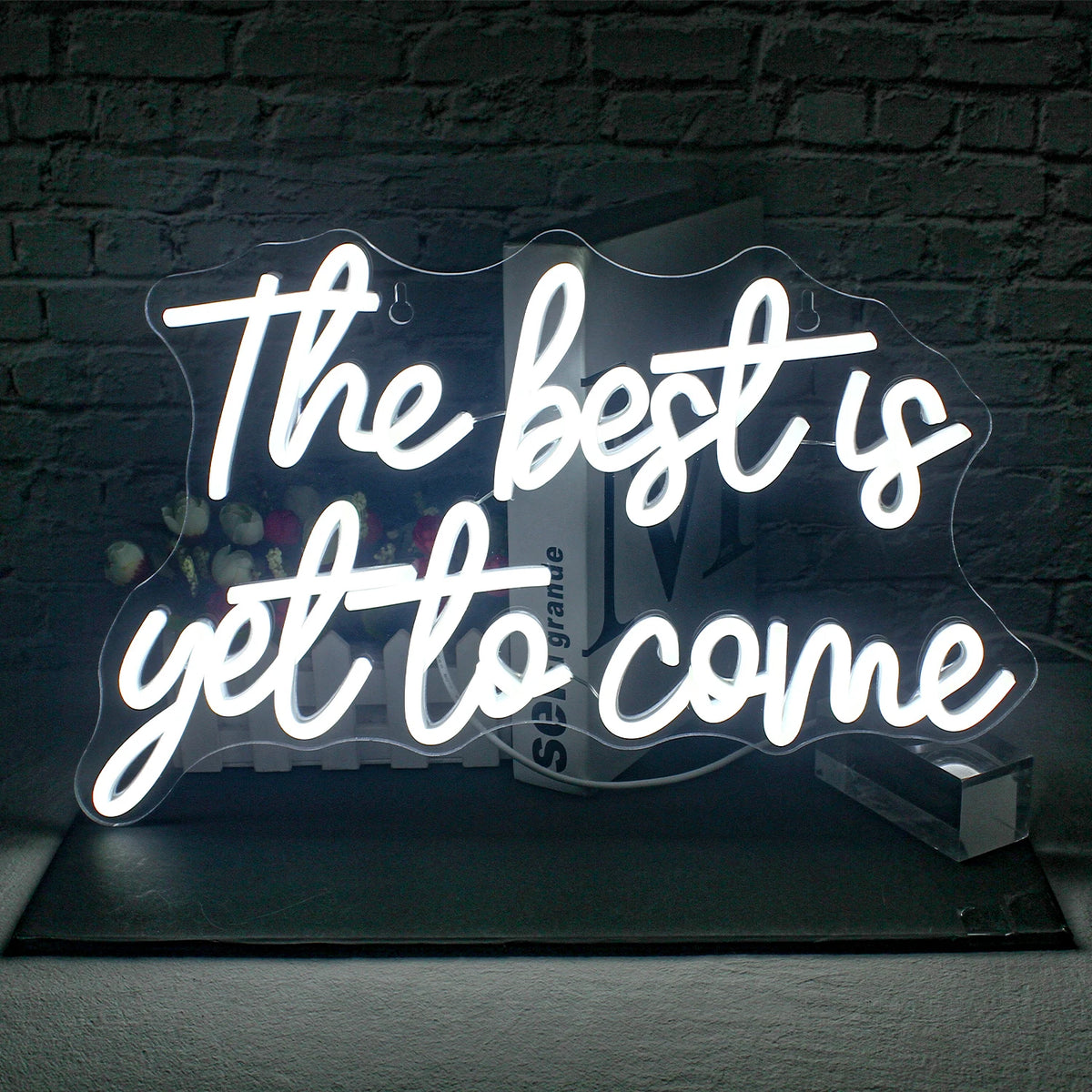De afbeelding toont een levendig, handgemaakt LED-neonbord met de tekst "The Best is Yet to Come" in een stijlvol, cursief lettertype.