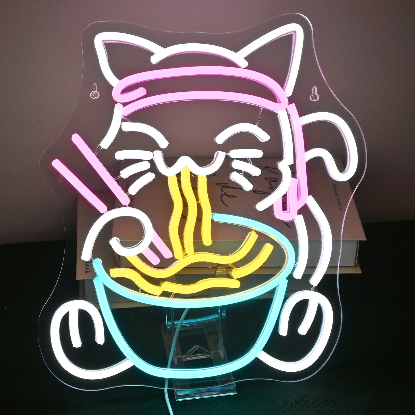 Op de afbeelding staat een levendig en kleurrijk LED-neonbord met een speels ontwerp van een kat die geniet van een kom ramen.
