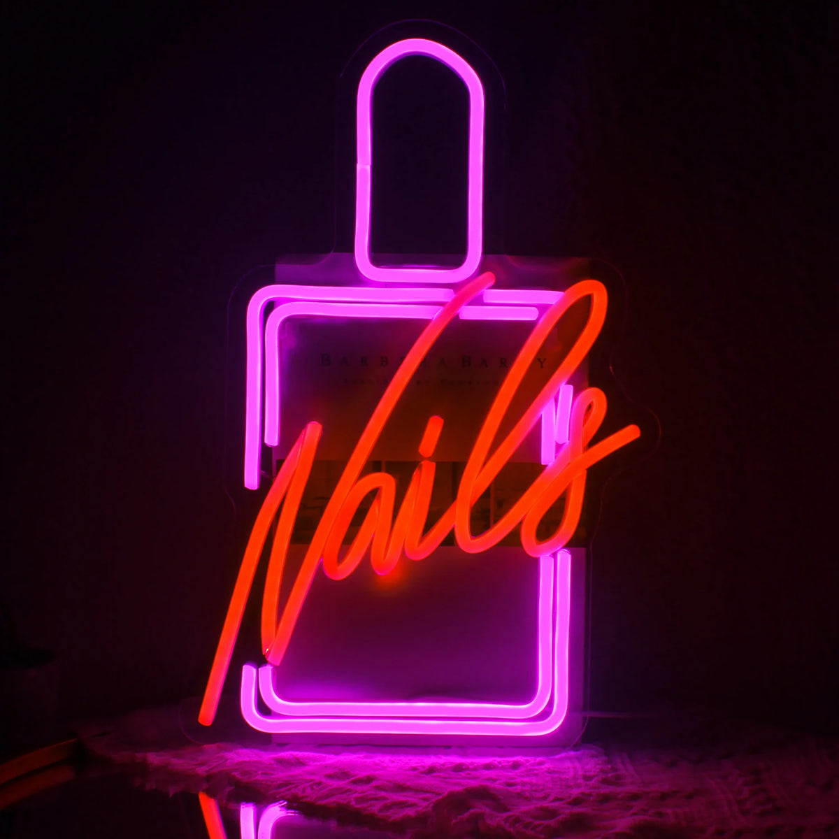 De afbeelding toont een levendig LED-neonbord waarop het woord "Nails" in een stijlvol, cursief lettertype staat.