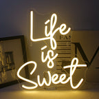The image features a vibrant, handmade LED neon sign in bright, glowing colors that spells out the phrase "Life is Sweet.