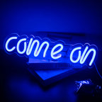 De afbeelding toont een levendig LED-neonbord met de tekst "Come On" in een opvallend en speels lettertype.