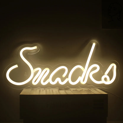 De afbeelding toont een levendig LED-neonbord in de vorm van het woord "Snacks" in een speels, cursief lettertype.