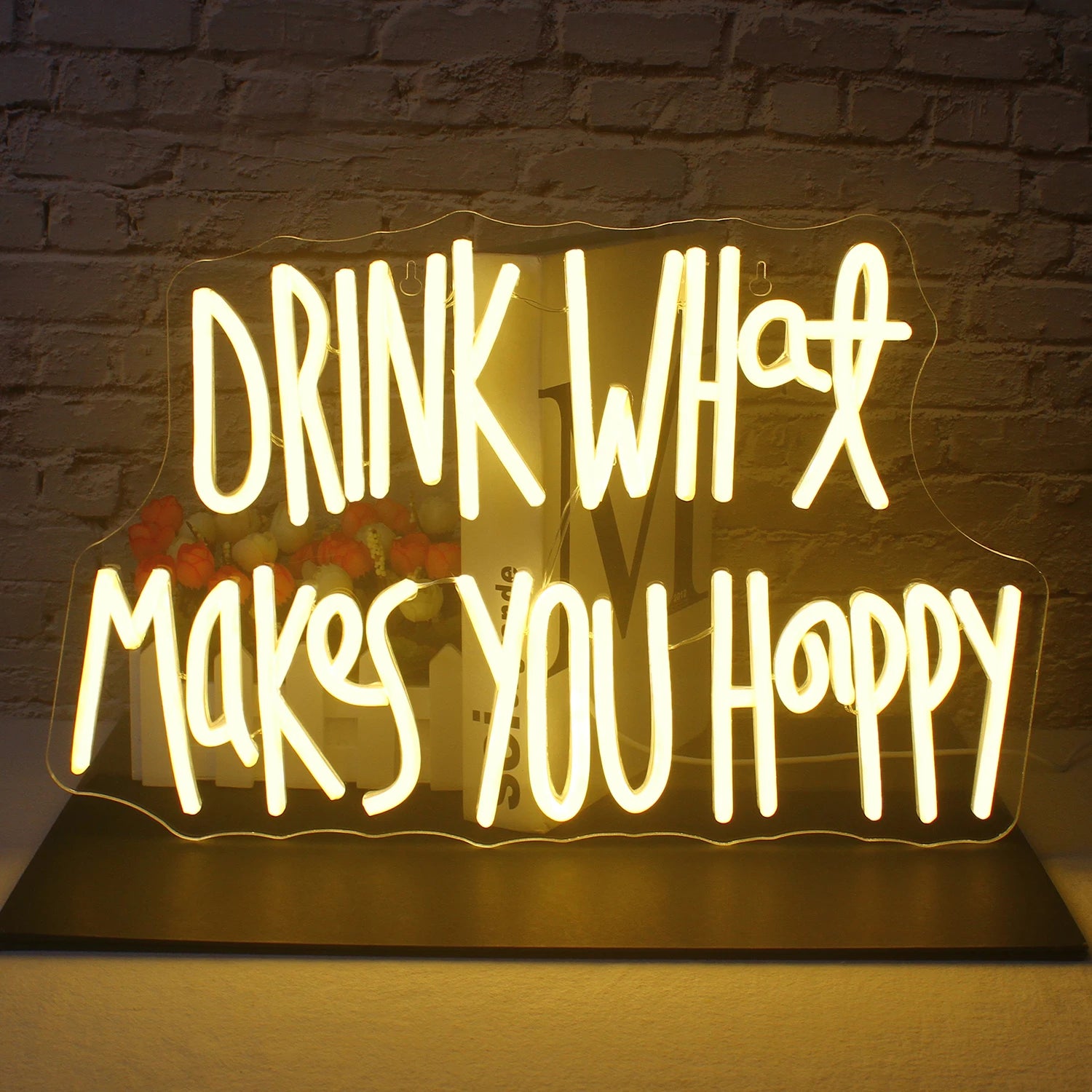 Op de afbeelding is een opvallend led-neonbord te zien met de tekst "Drink What Makes You Happy" in een elegant, cursief lettertype.