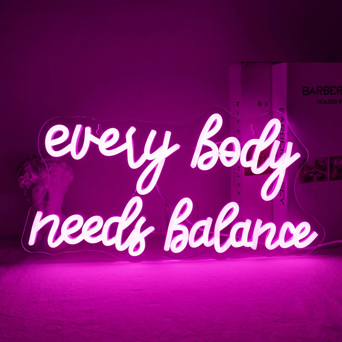 Op de afbeelding is een levendig LED-neonbord te zien met de tekst "Every Body Needs Balance".