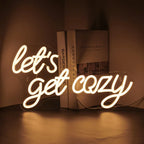 De afbeelding toont een levendig LED-neonbord met de tekst "Let's Get Cozy" in een warm, uitnodigend lettertype.