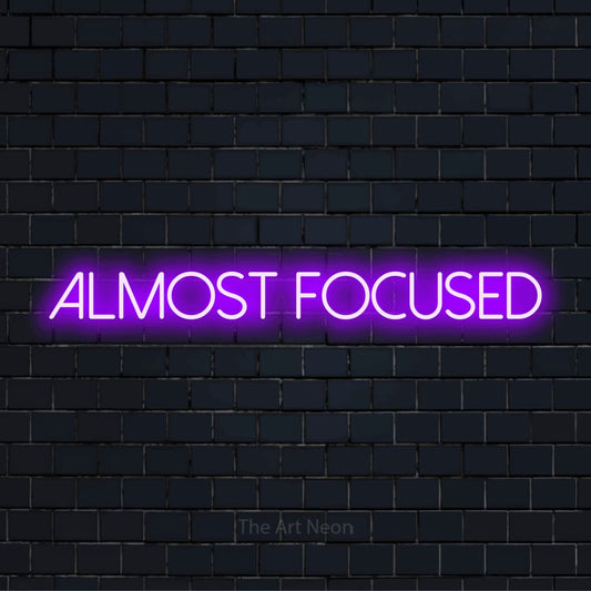 "Almost Focused" neon text design on a black brick wall