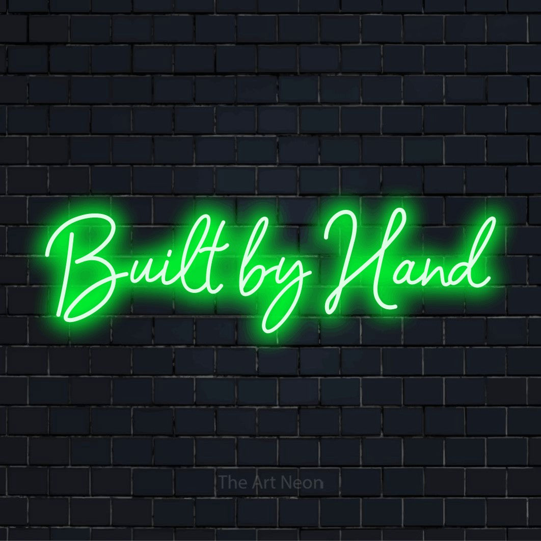 "Built By Hand" neon text design on a black brick wall