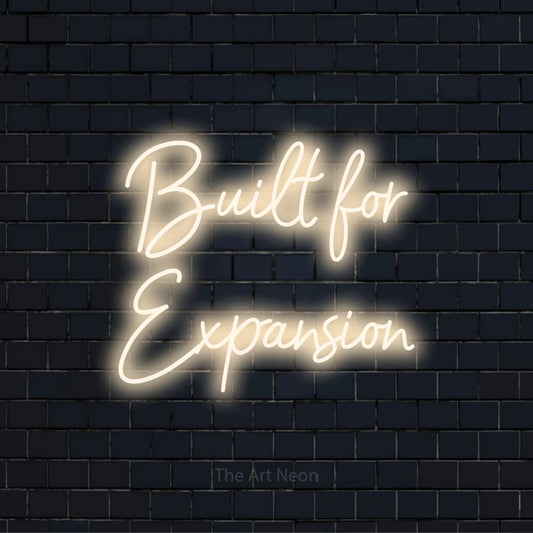 "Built For Expansion" glowing LED neon sign on a black brick wall