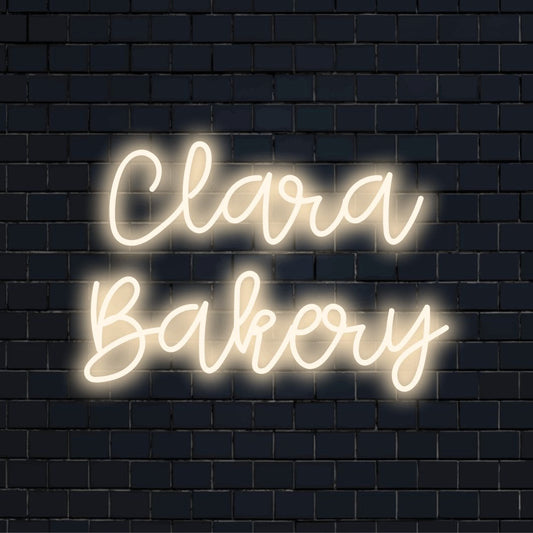Clara Bakery Custom Name Neon Sign, glowing lettering against brick backdrop