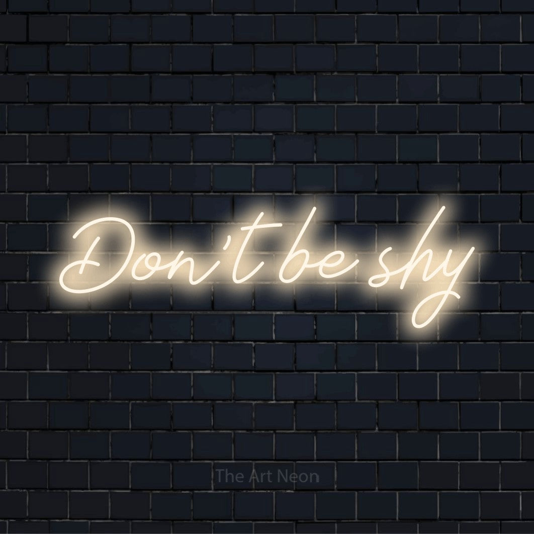 "Don’t Be Shy" LED neon sign on a black brick wall