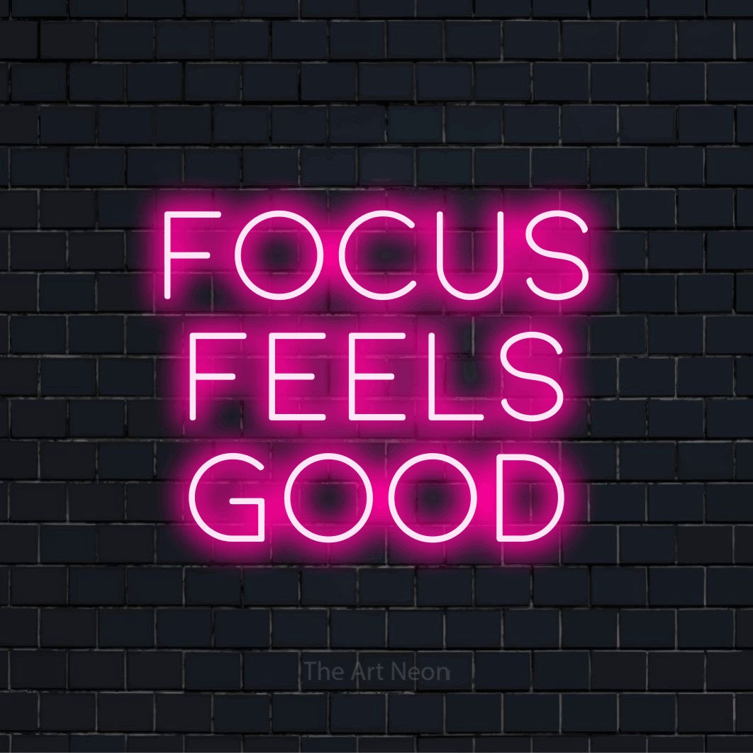 "Focus Feels Good" script-style LED neon sign on a black brick wall