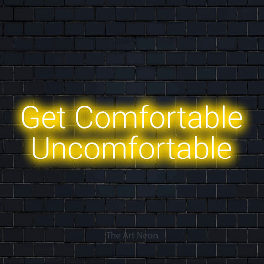 "Get Comfortable Uncomfortable" script-style LED neon sign on a black brick wall