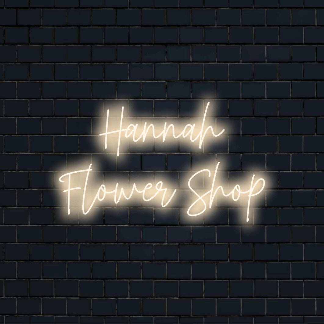 Hannah Flower Shop Personalized Neon Light with glowing lettering against black brick wall