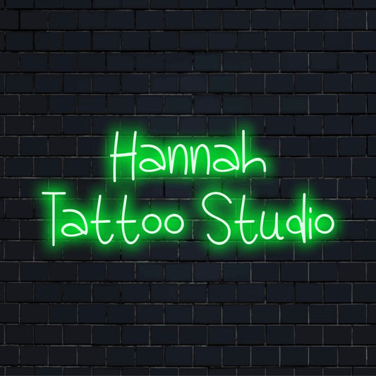 Hannah Tattoo Studio Custom Name Neon Sign, glowing lettering on dark brick wall