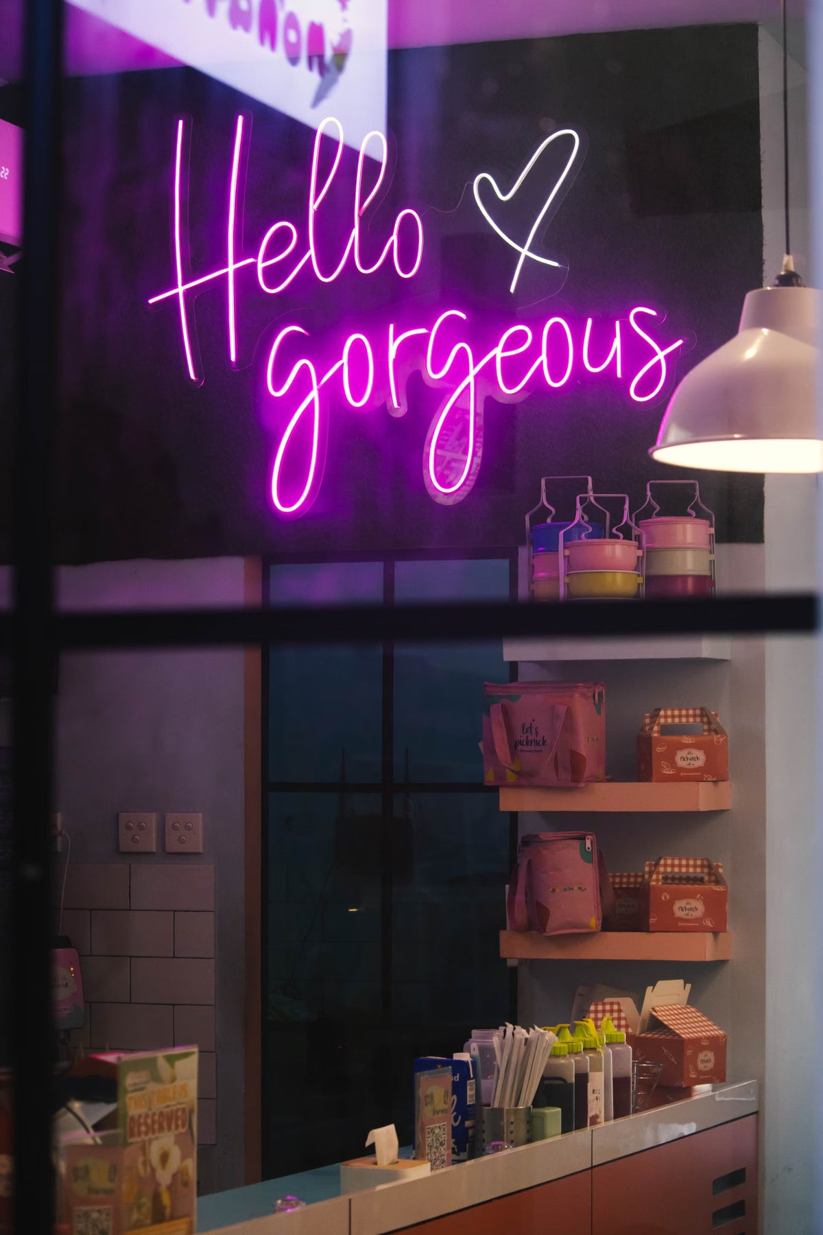 Pink Hello Gorgeous LED neon sign displayed behind a retail shop window
