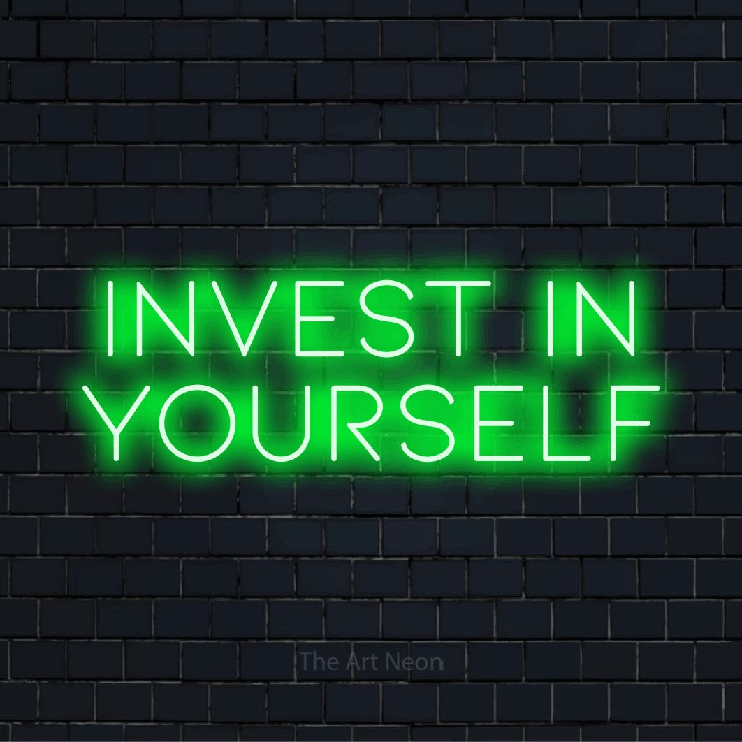 "Invest In Yourself" script-style LED neon sign on a black brick wall