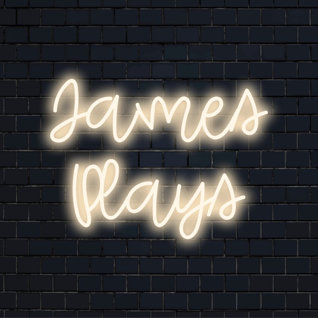James Plays Custom Name Neon Sign, bright neon lettering on dark brick background