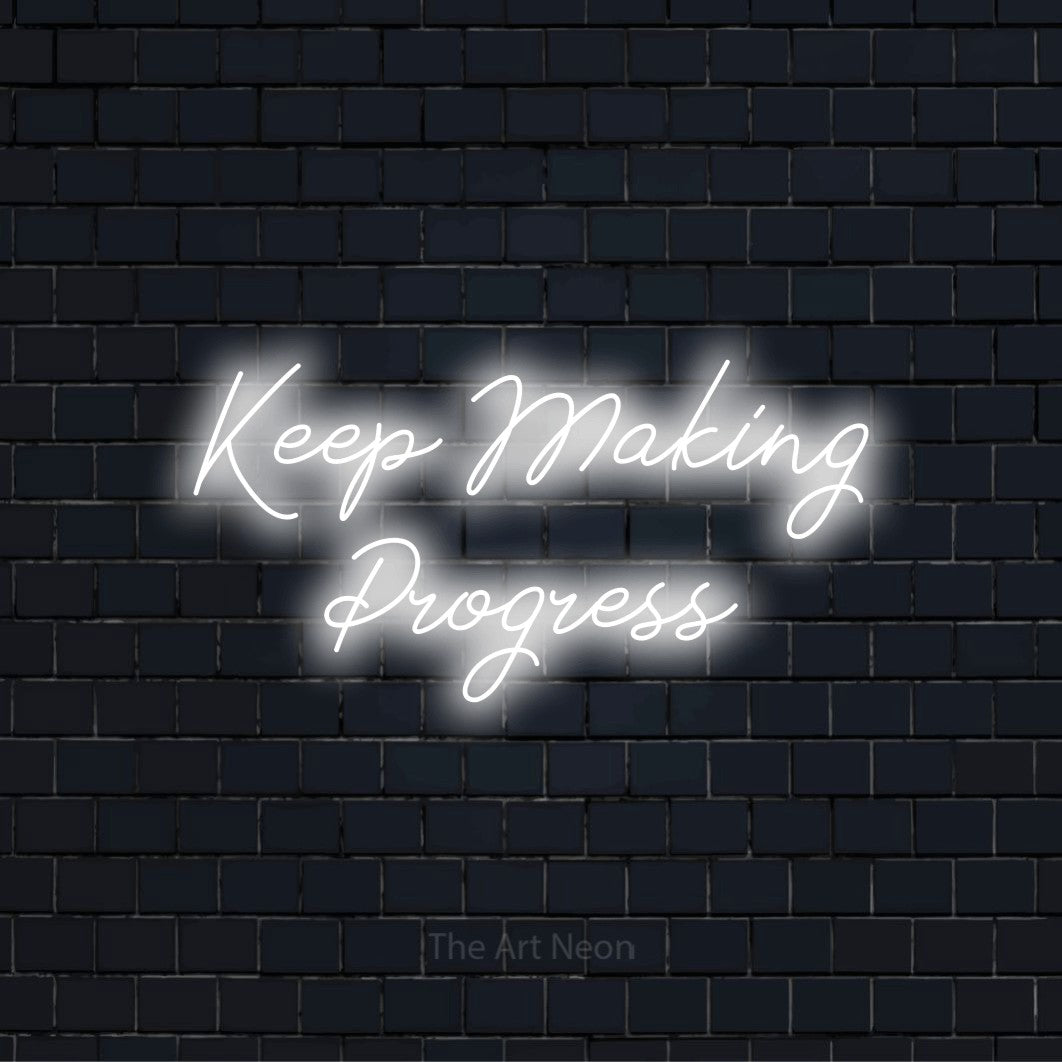"Keep Making Progress" script-style LED neon sign on a black brick wall