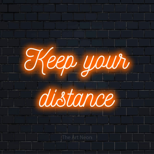 "Keep Your Distance" script-style LED neon sign on a black brick wall