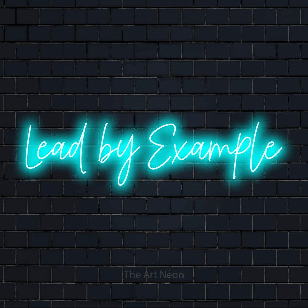"Lead By Example" script-style LED neon sign on a black brick wall