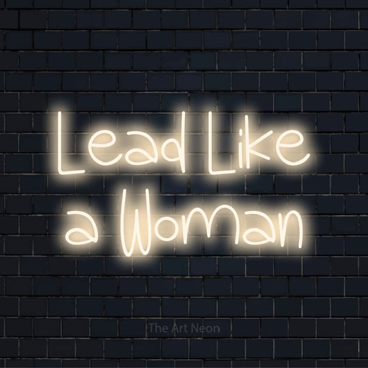 "Lead Like A Woman" glowing LED neon sign on a black brick wall
