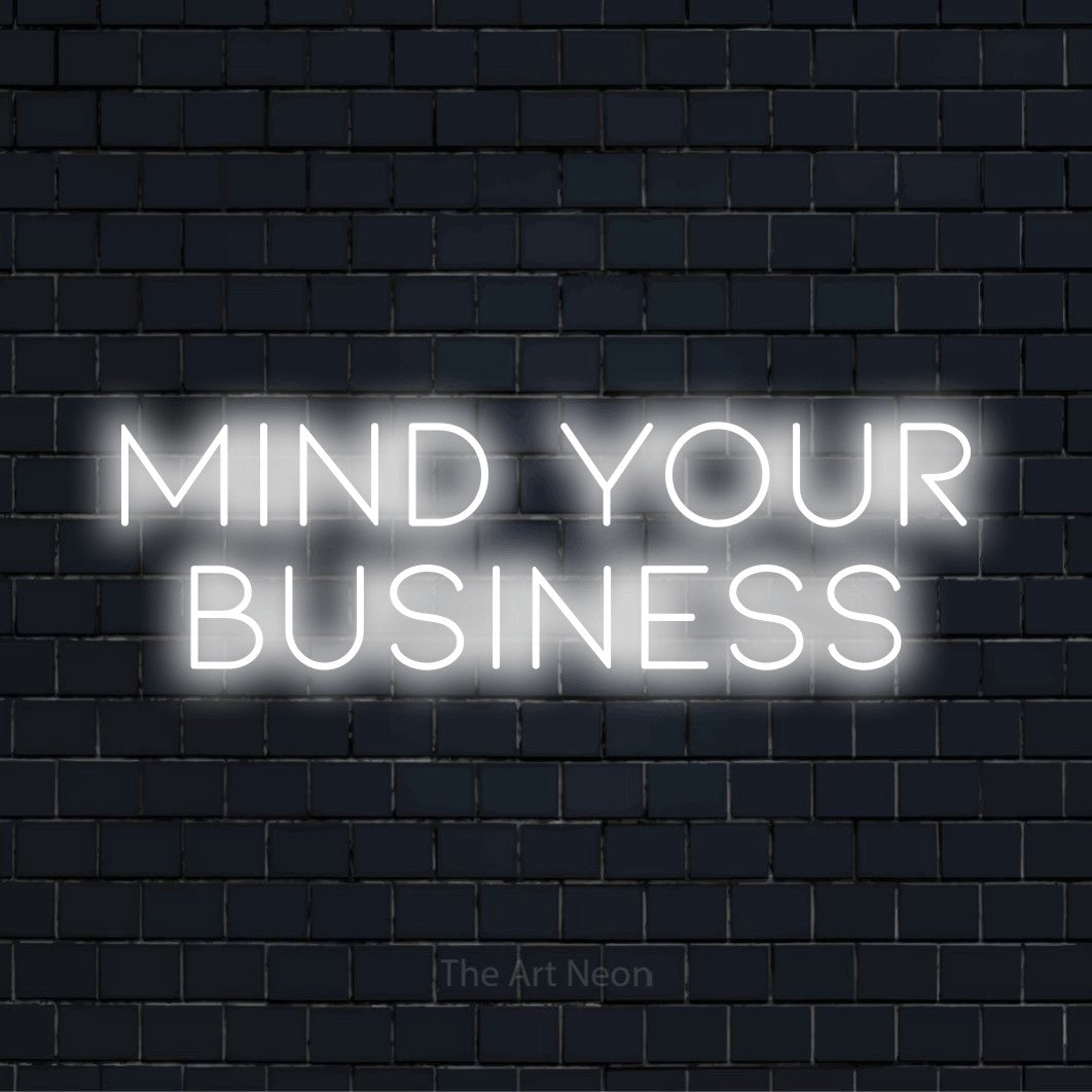 "Mind Your Business" script-style LED neon sign on a black brick wall