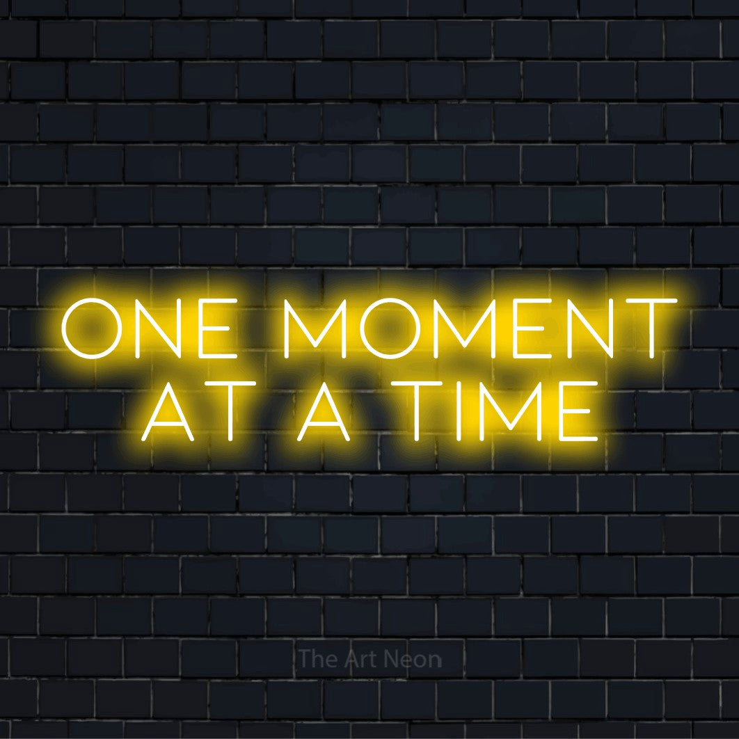 "One Moment At A Time" LED neon sign on a black brick wall