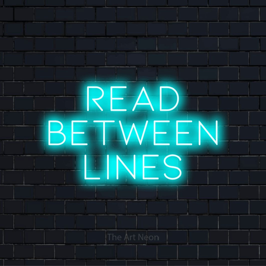 "Read Between Lines" script-style LED neon sign on a black brick wall
