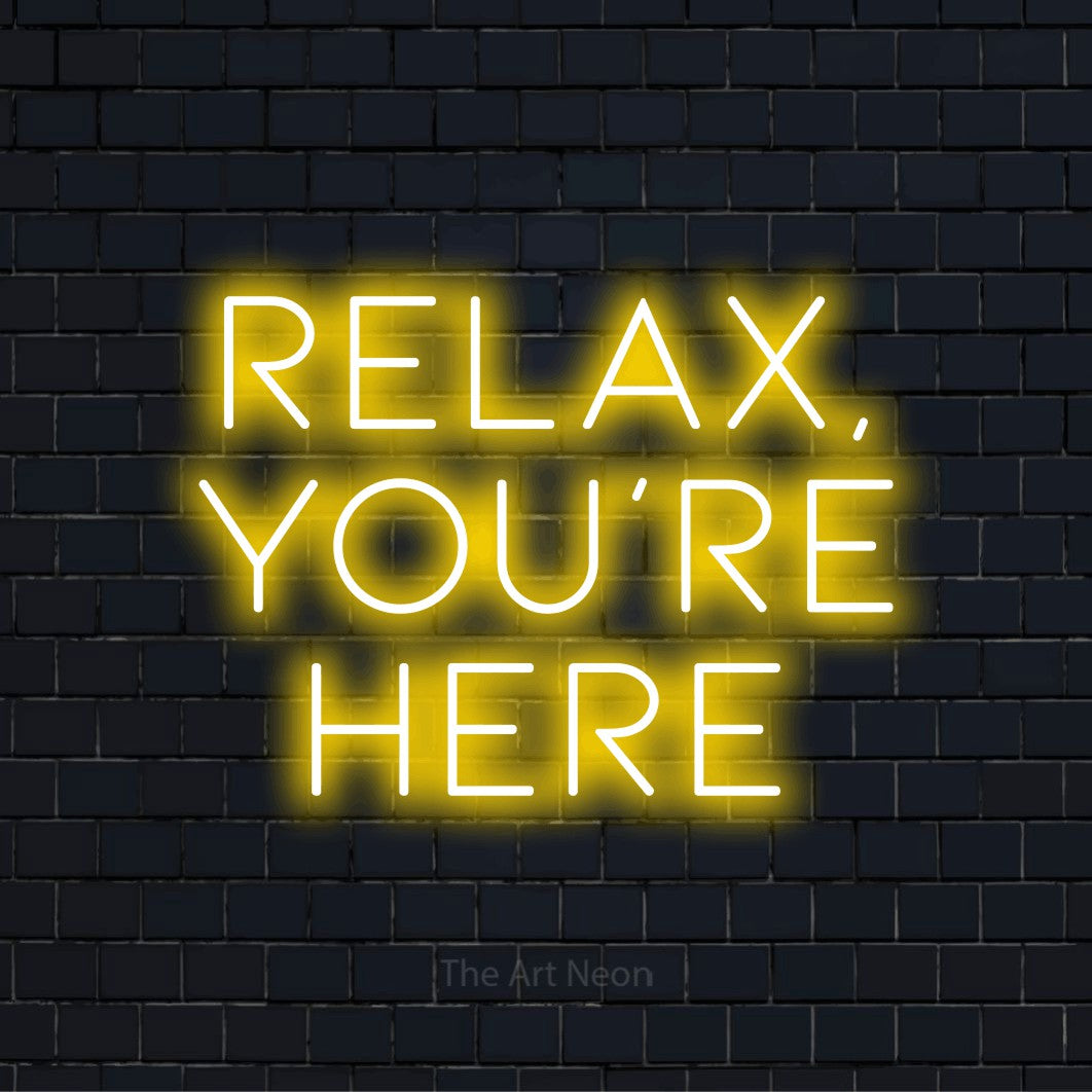 "Relax, You’re Here" LED neon sign on a black brick wall