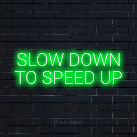 "Slow Down To Speed Up" text design with neon effect on a black brick wall