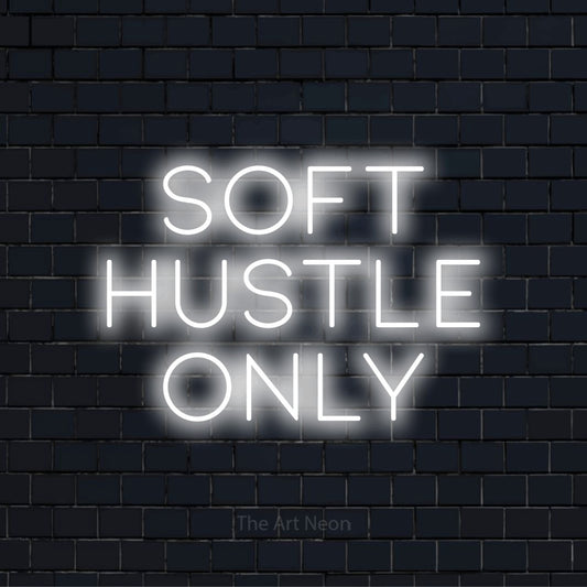 "Soft Hustle Only" script-style LED neon sign on a black brick wall