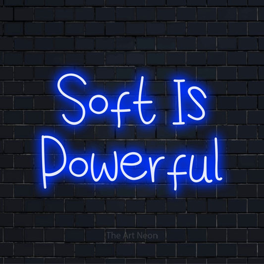 "Soft Is Powerful" script-style LED neon sign on a black brick wall
