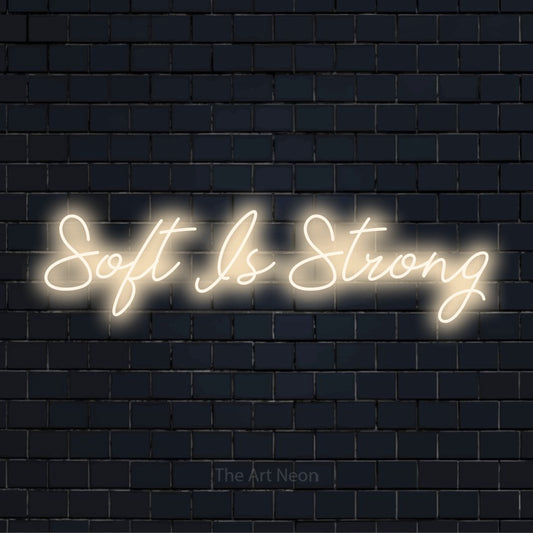 "Soft Is Strong" LED neon sign on a black brick wall
