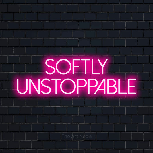 "Softly Unstoppable" LED neon sign on a black brick wall