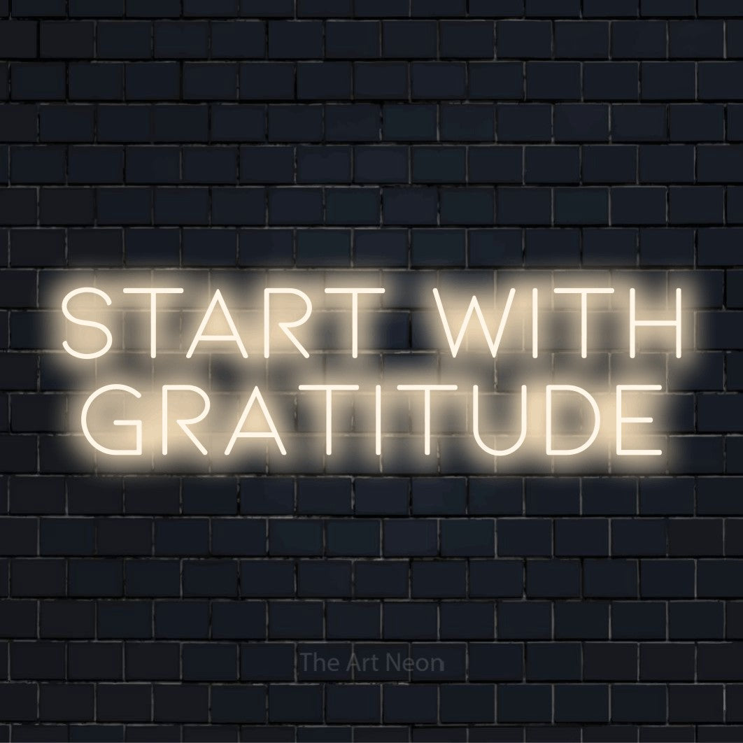 "Start With Gratitude" glowing LED neon sign on a black brick wall